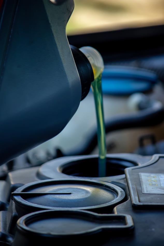 An auto mechanic changing oil pours oil into a car engine.